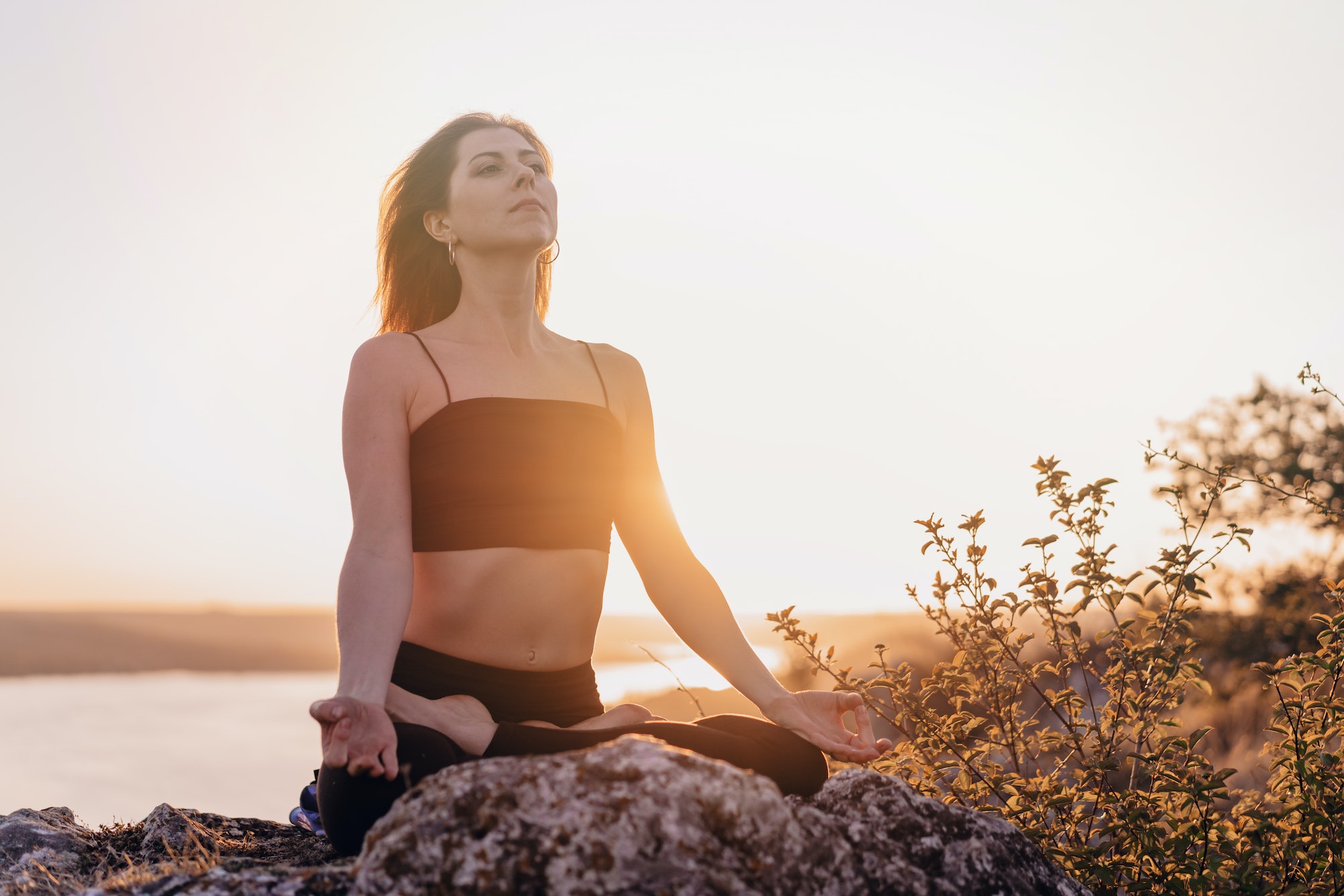 Peaceful yogi woman sitting in lotus, meditating, feeling free in front of wild nature.